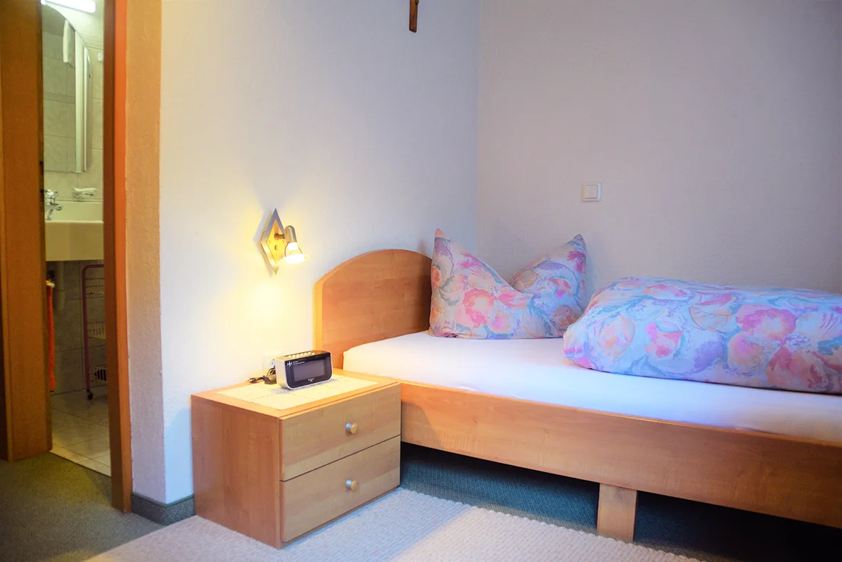 Einzelzimmer mit Einzelbett, Nachttisch und offener Tür zum eigenen Bad