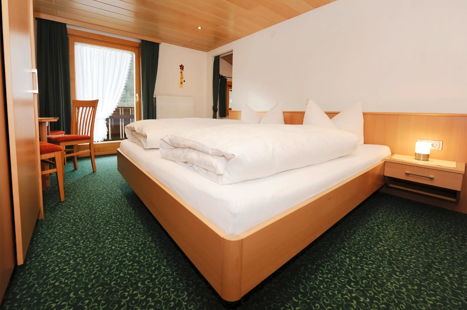Schlafraum im Komfortzimmer mit Doppelbett, Holzdecke und Balkontür