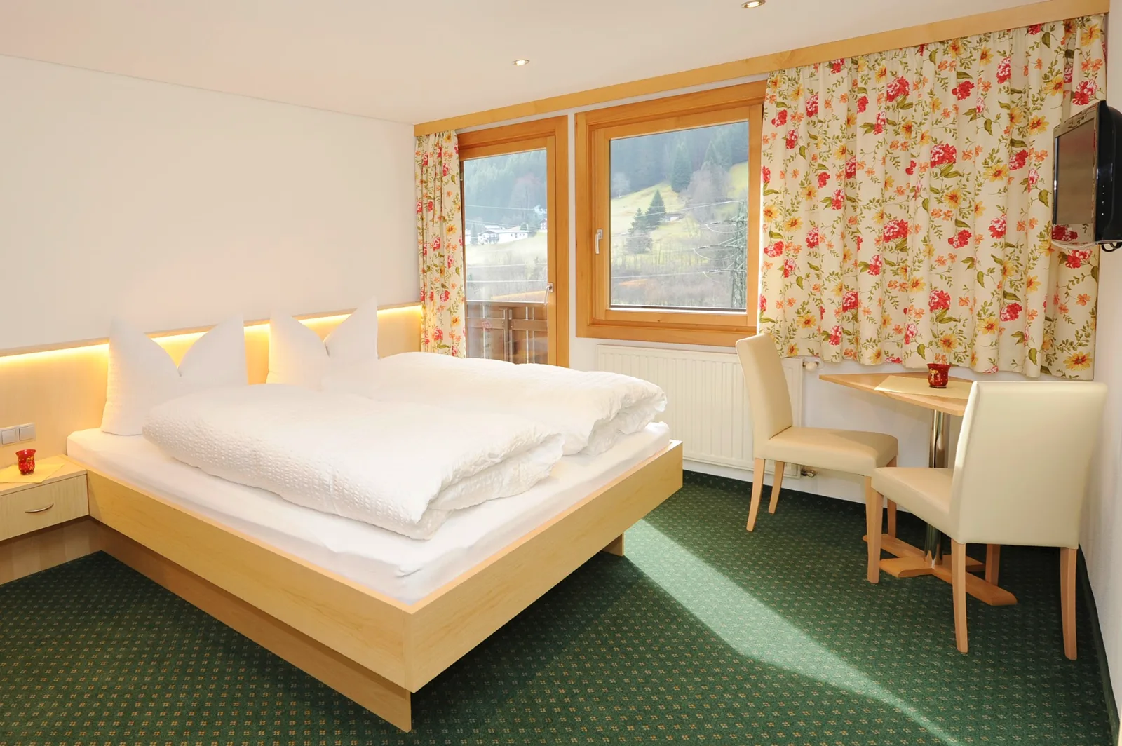Doppelzimmer mit zwei Fenstern, Tisch am Fenster und Blick auf den bewaldeten Hang